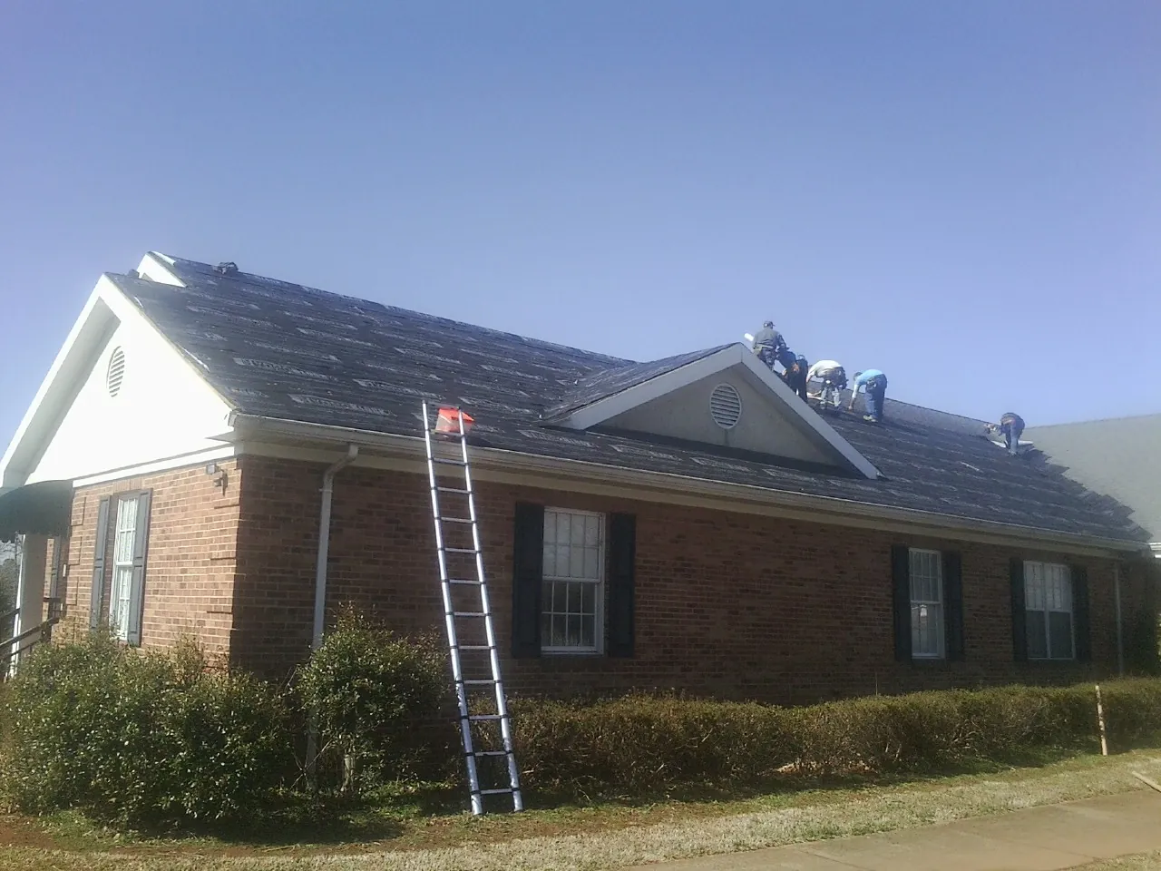 Crew tearing shingles off a brick ranch roof with a ladder set — Emergency Roof Repair work by our crew in Cookstown