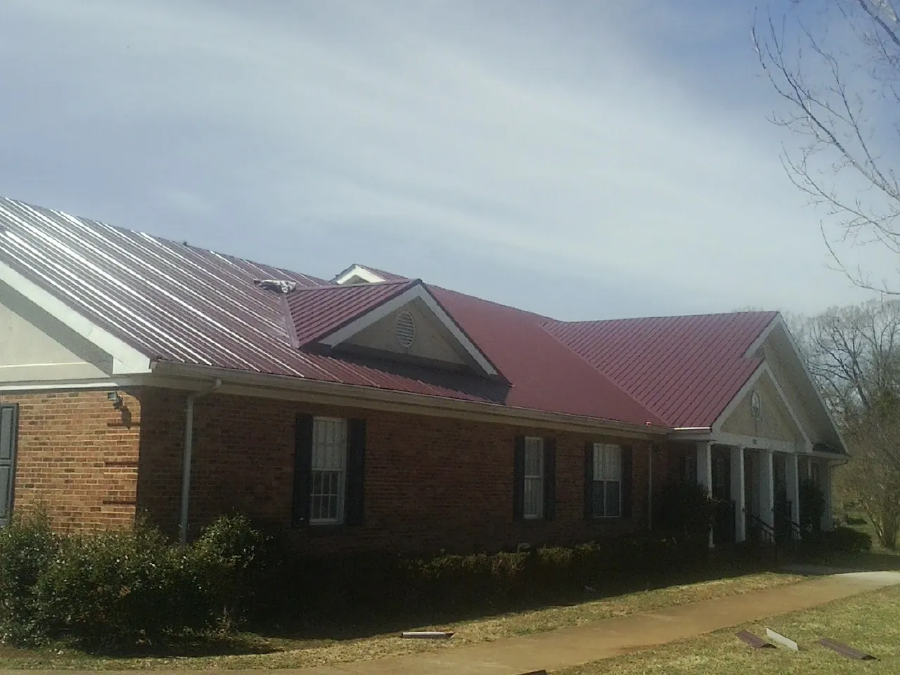 Red metal roof with gabled entries on a long brick building, from a Hail Damage Roof Repair job in Cookstown
