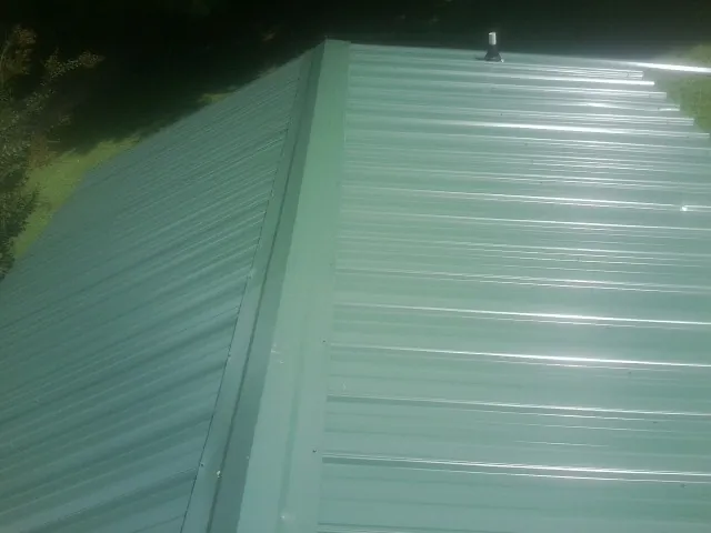 New green metal panels meeting at the ridge of a roof — Flat Roof Repair work by our crew in Cookstown