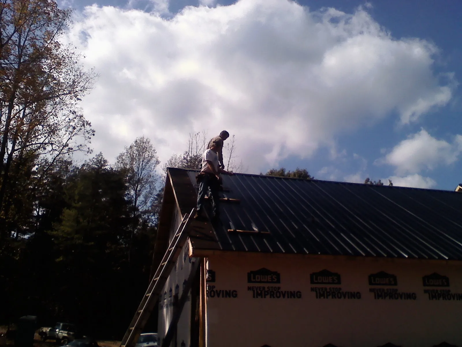 Roofer fastening dark metal panels high against a cloudy sky, from a Roof Inspection job in Cookstown