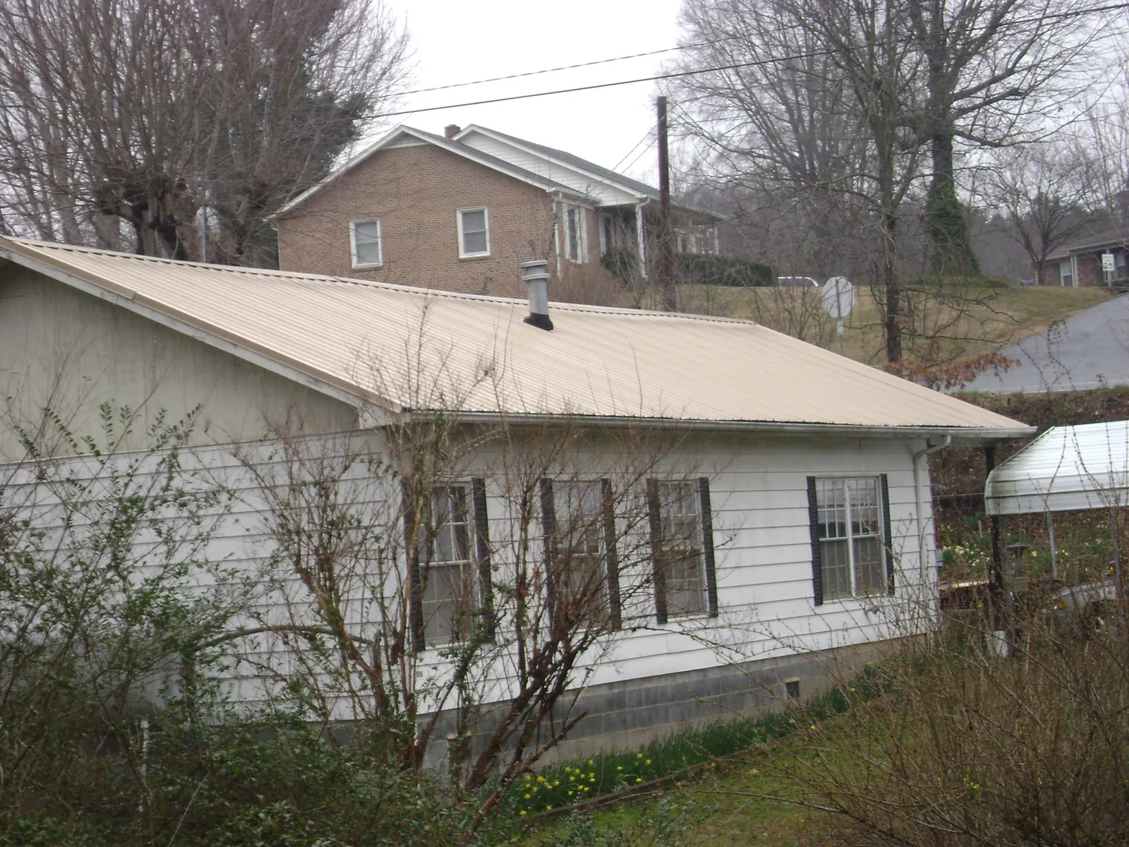 Tan metal roof on a white sided house set into a hillside — Commercial Roofing by Roofing Brothers in Cookstown