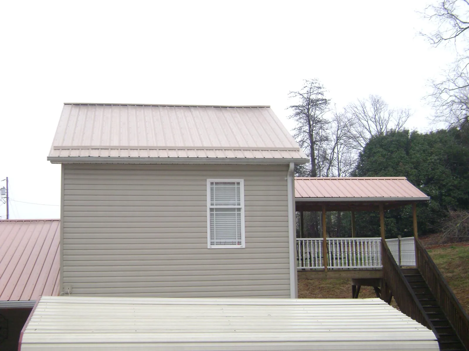 Tan metal roofs on a two story addition and attached porch, from a Roof Replacement job in Cookstown